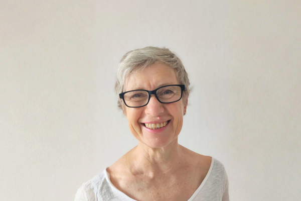 Porträtfoto von Lisa Thomas. Sie hat kurze graue Haare, trägt eine dunkle Hornbrille und eine weißes T-Shirt.