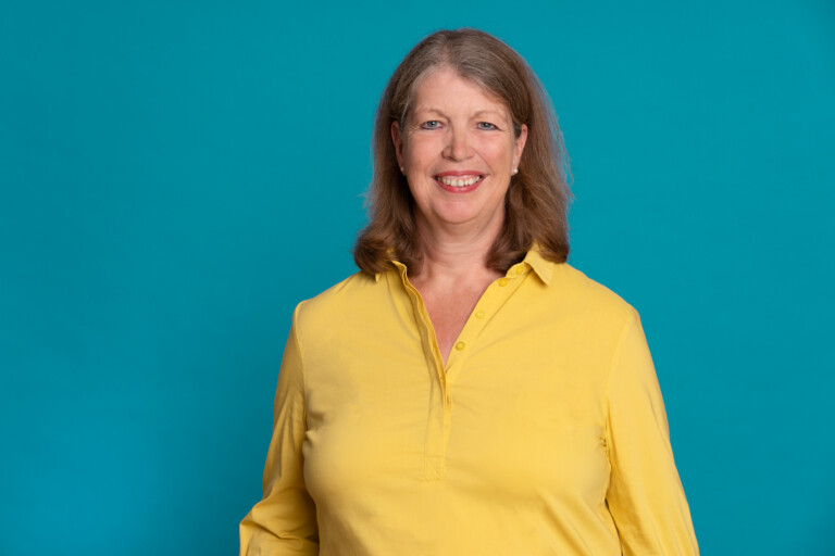 Portrait photo of Almuth Fricke in a yellow blouse against a turquoise background