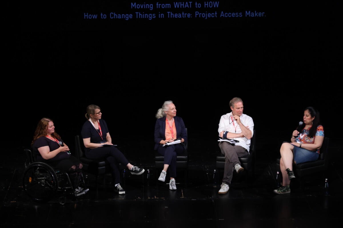 Auf einer Bühne sitzen nebeneinander fünf Personen. Die Person ganz links, Roisin Keßler, sitzt im Rollstuhl.