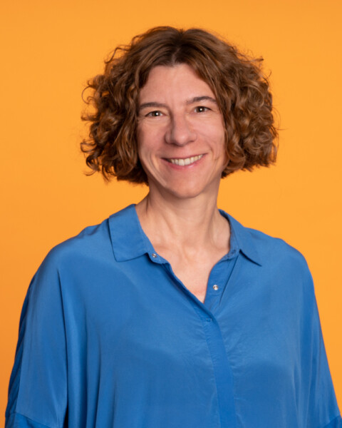 Woman with curly hair wearing blue shirt against orange background