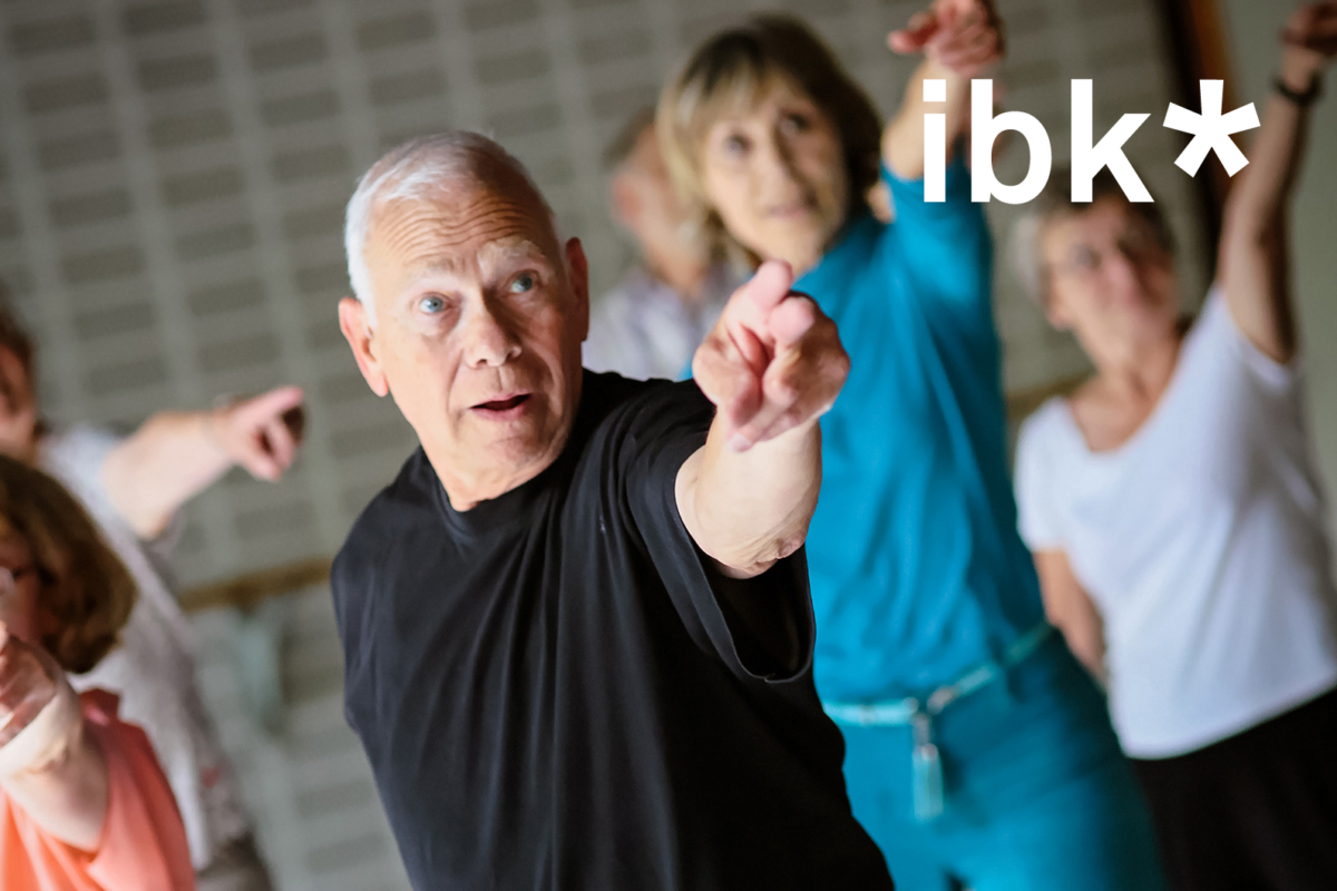 An elderly man in a group of people who all seem to be pointing at the ibk logo (photomontage).