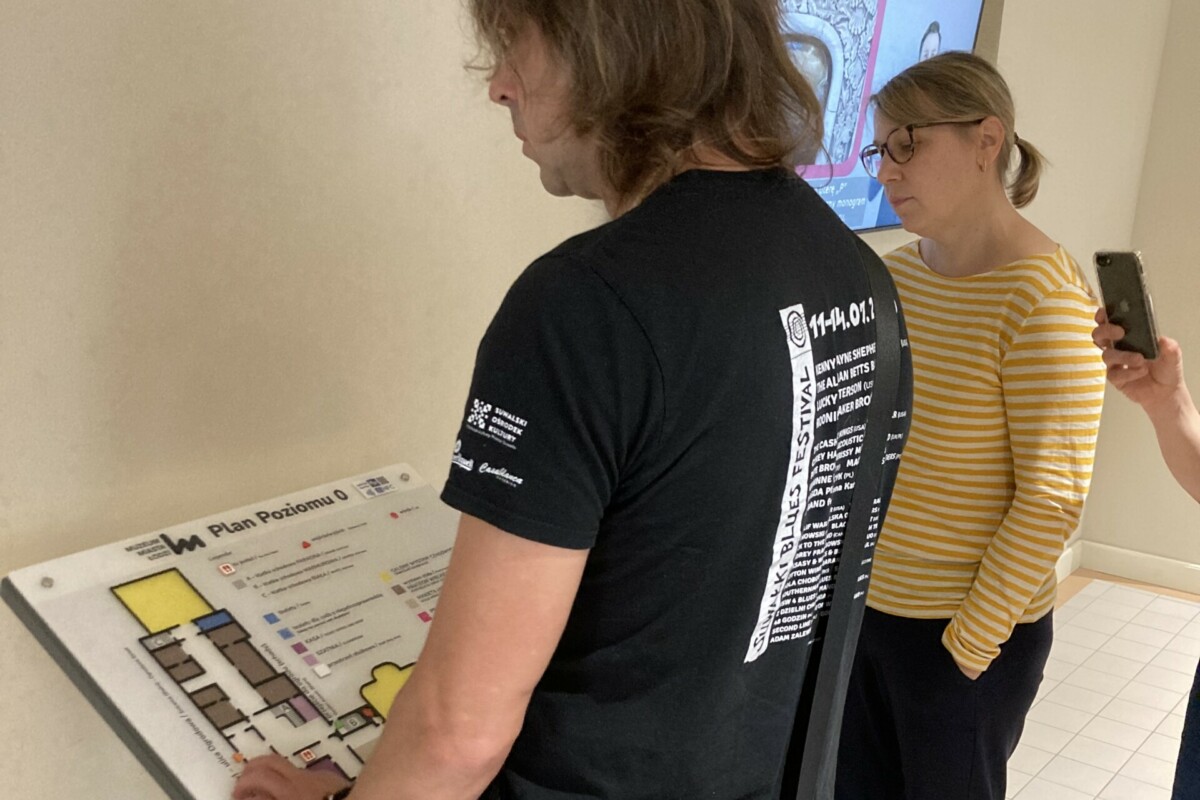 A man with a blind man's stick stands in front of a tactile model of a room plan and feels it.