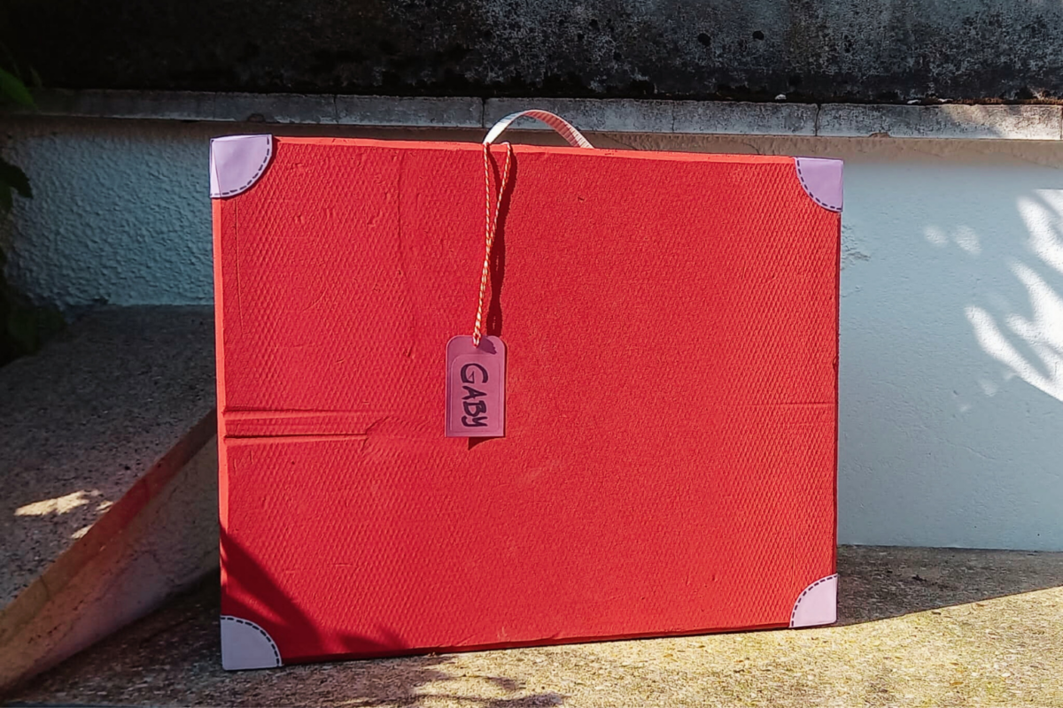 Ein roter, aus Pappkarton gebastelter Koffer mit einem Anhänger