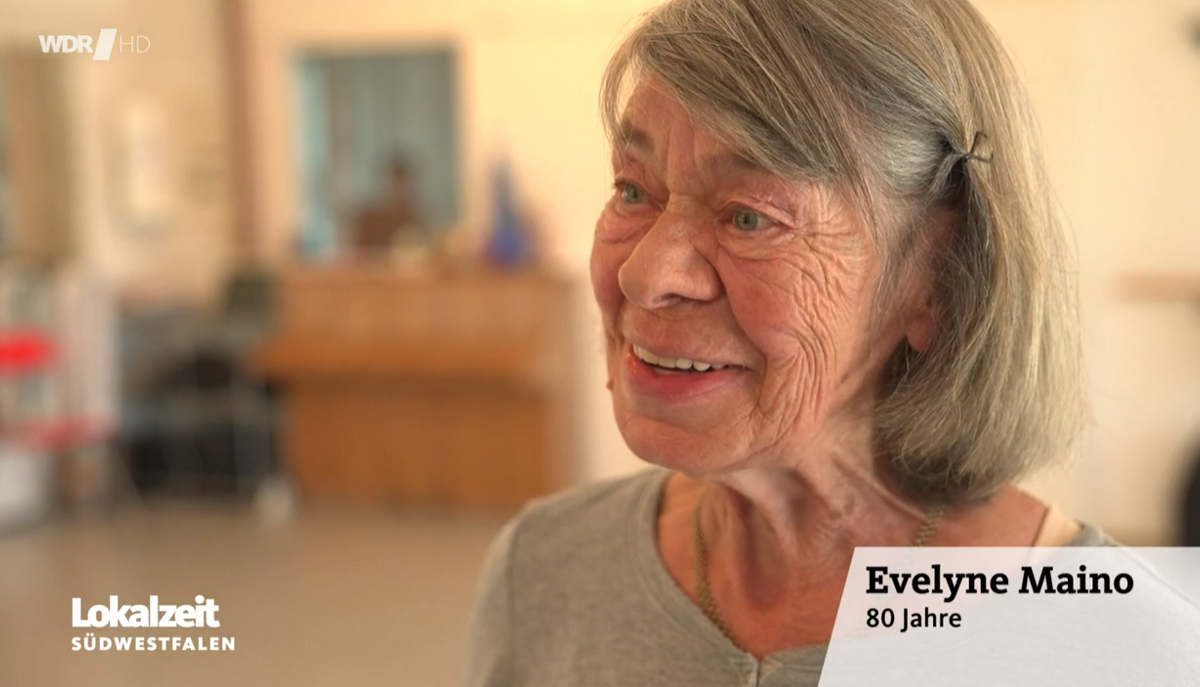 Eine lächelnde alte Frau mit der Beschriftung "Evelyne Maino, 80 Jahre"