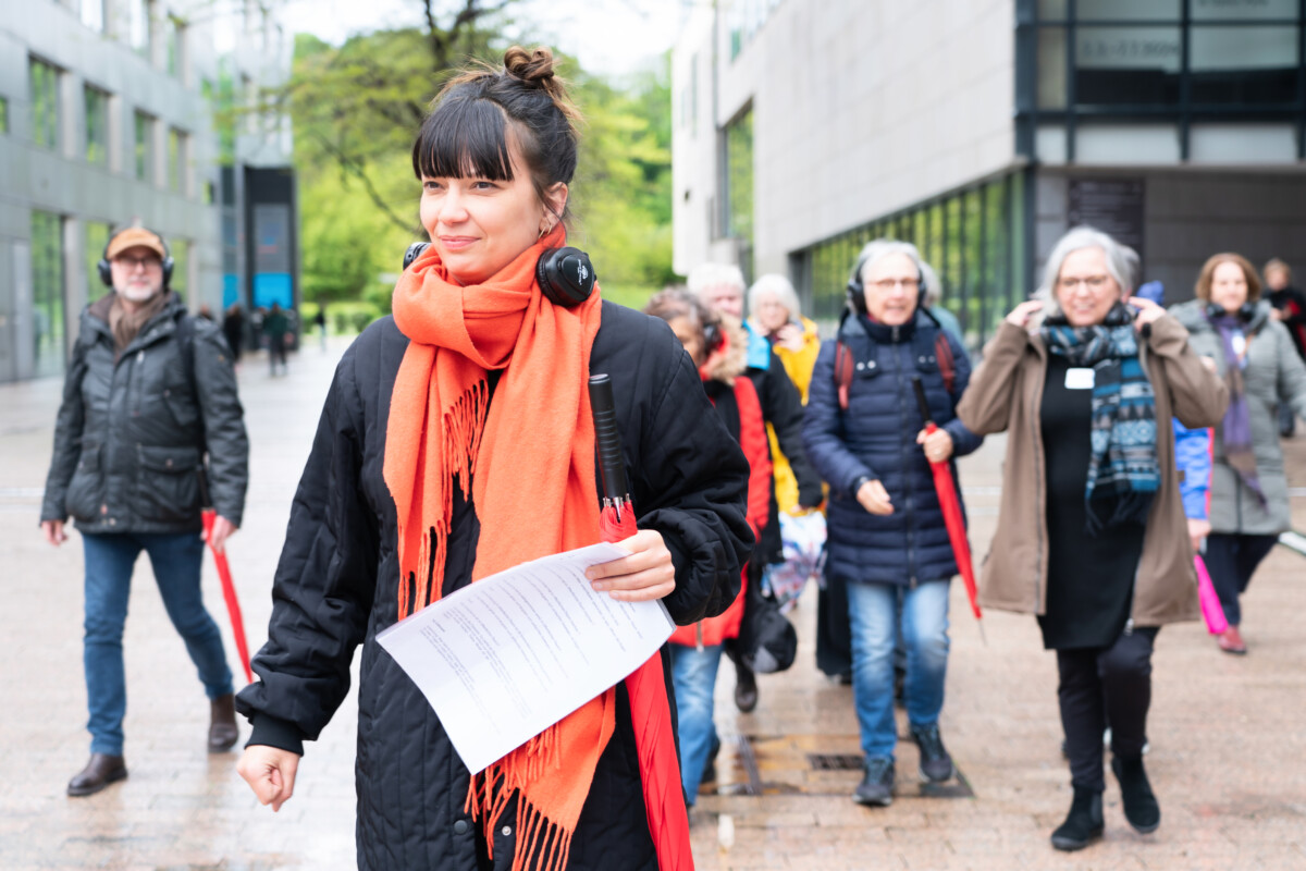 Eine Frau mit einem Blatt in der Hand und eine Gruppe von Menschen, die spazieren gehen