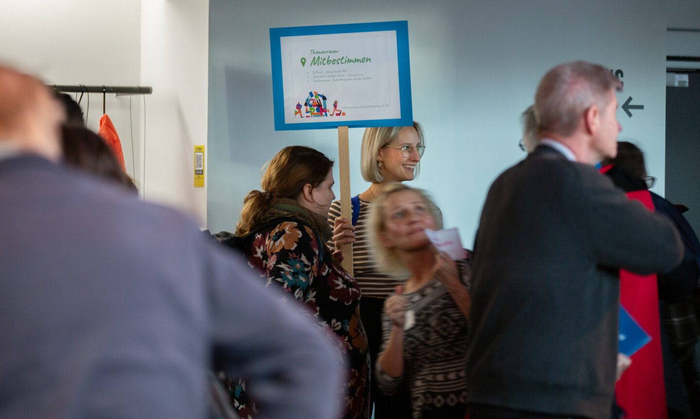 Eine Gruppe von Menschen, die sich um ein Schild mit der Aufschrift "Themenraum Mitbestimmen" gruppieren