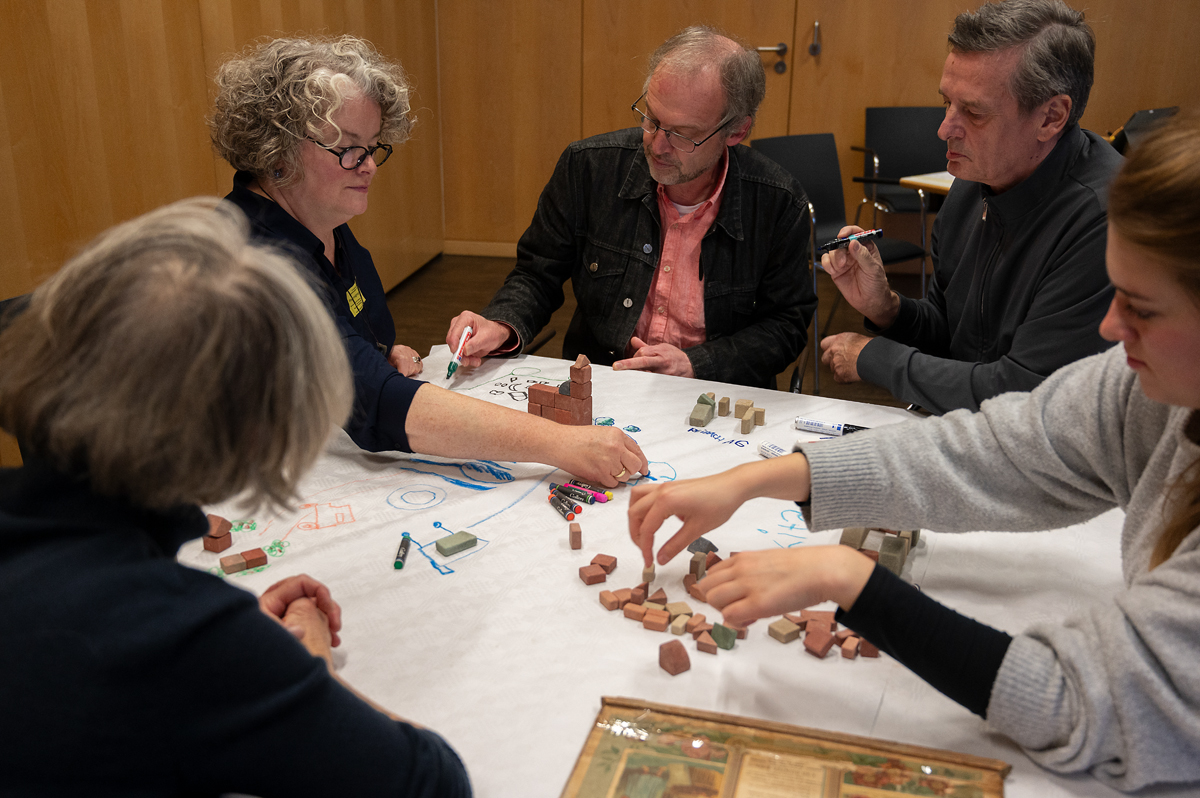 Workshop-Teilnehmende sitzen um einen Tisch sitzen und arbeiten mit Stein-Bauklötzen.