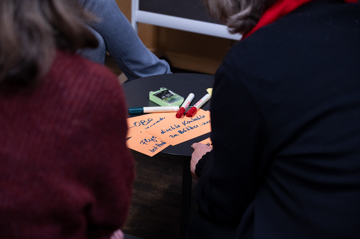 Beschriftete Moderationskarten liegen auf einem Tisch, um den mehrere Personen sitzen.