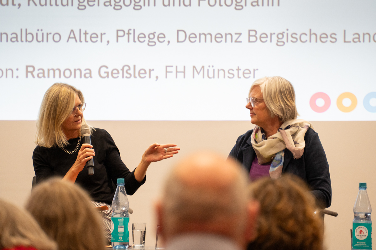 Zwei Frauen sitzen nebeneinander. Die eine spricht in ein Mikrofon.