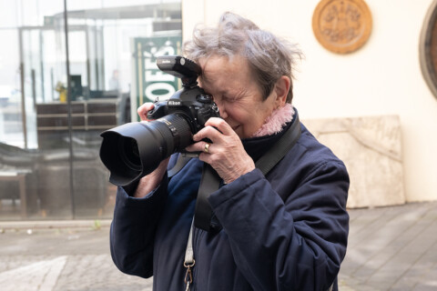 Eine ältere Frau hält eine große Fotokamera in den Händen und schaut durch den Sucher.