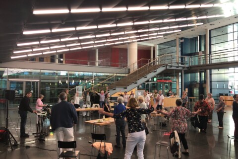 Mehrere Personen stehen in einem großen Saal verteilt und bewegen ihre Arme