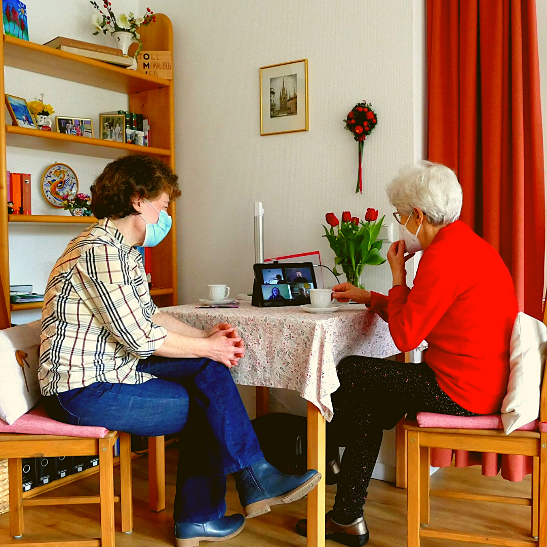 Zwei Frauen sitzen an einem Tisch und schauen auf ein Tablet.