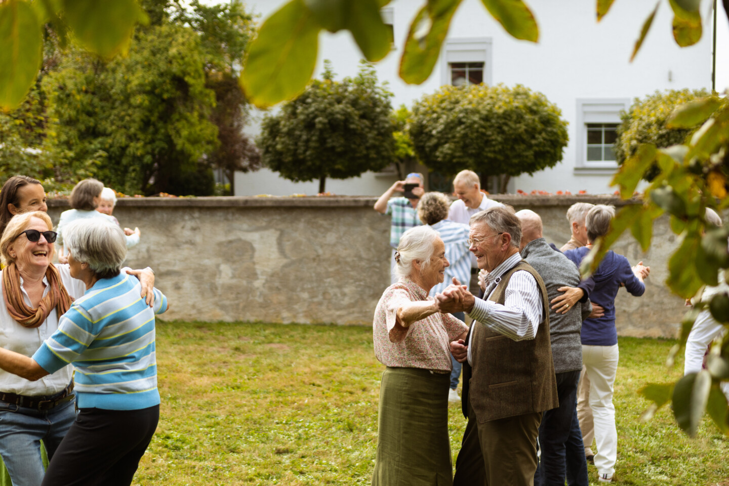 Fotografie: Ältere Menschen tanzen paarweise auf einer Wiese.