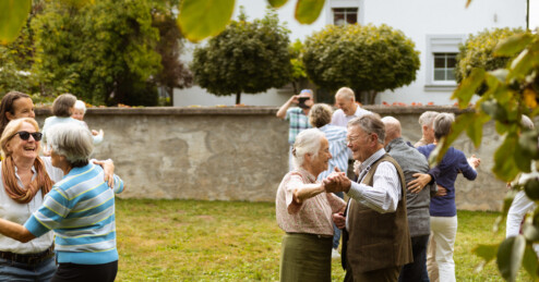 Fotografie: Ältere Menschen tanzen paarweise auf einer Wiese.