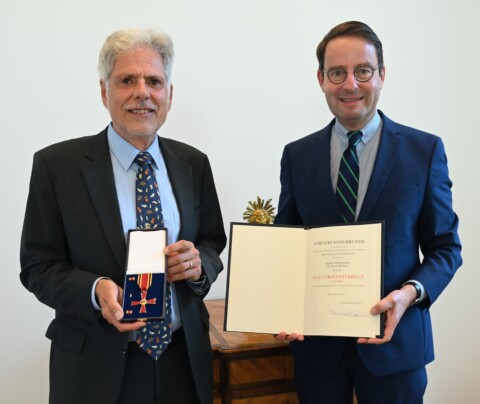Prof. Dr. Hans Hermann Wickel und Regierungspräsident Andreas Bothe bei der Verleihung des Bundesverdienstkreuzes. Wickel zeigt den Orden, Bothe präsentiert die Urkunde.