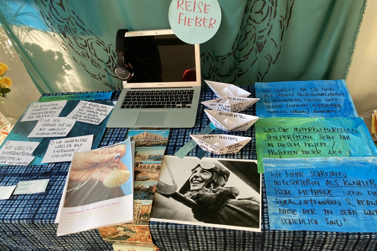 Auf einem Tisch liegen blau-grüne Materialien und Fotos zu dem Projekt. Auf einem Laptop kann ein Film angeschaut werden.