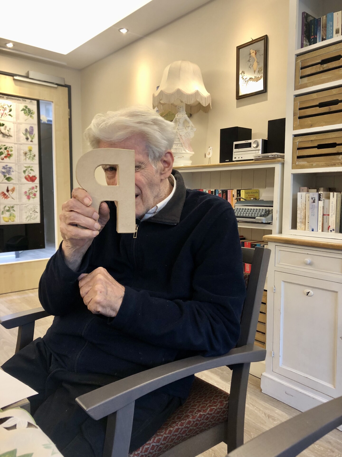 Ein älterer Mann hält lachend einen Pappbuchstaben vor sein Gesicht.