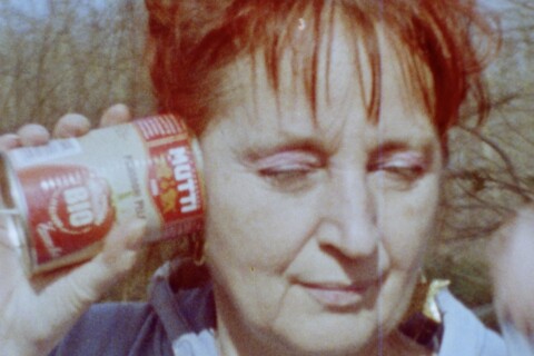 Selbstporträt der Künstlerin Dagie Brundert: Eine rotharige Frau hält sich eine geöffnete Dose mit rotem Etikett und der Aufschrift „BIO“ und „Tomaten“ ans Ohr. Im Hintergrund stehen kahle Bäume.