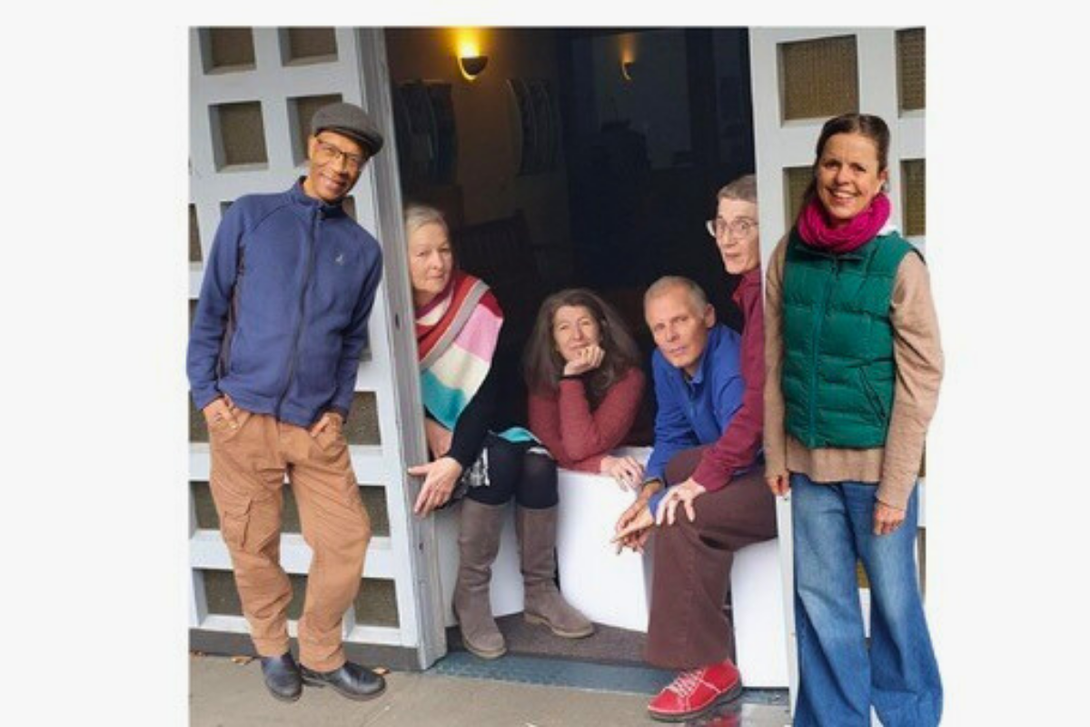 Gruppenfoto von fünf Personen, die Im Eingangsbereich eines Gebäudes sitzen und stehen.