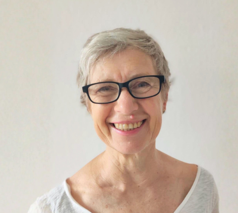 Porträtfoto von Lisa Thomas. Sie hat kurze graue Haare, trägt eine dunkle Hornbrille und eine weißes T-Shirt.