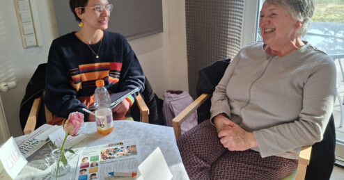 Eine junge und eine alte Frau sitzen am Tisch in einem Stadtteilzentrum und sind im Dialog.