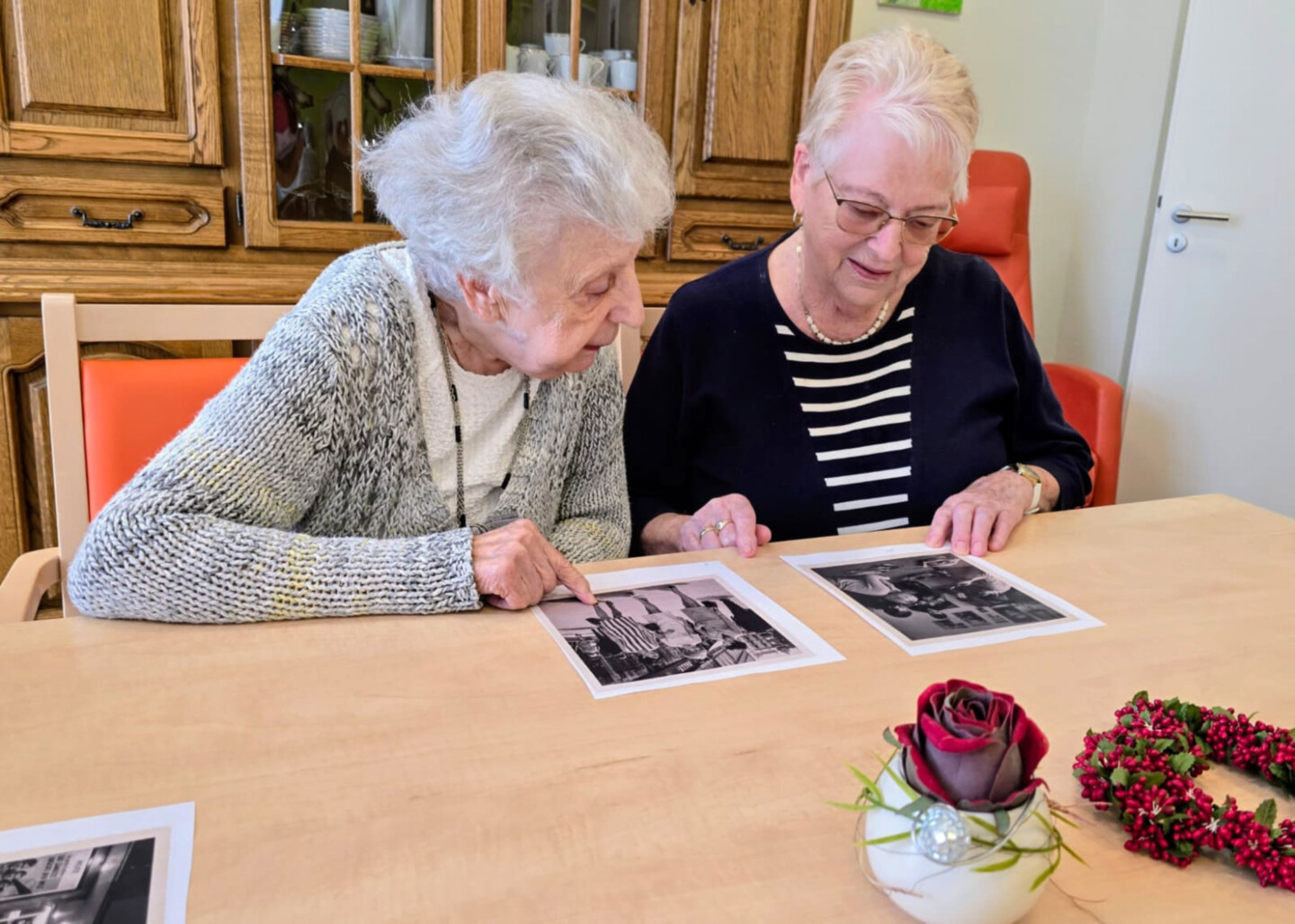 Zwei ältere Frauen betrachten schwarz-weiß Fotografien, die vor Ihnen auf einem Tisch liegen