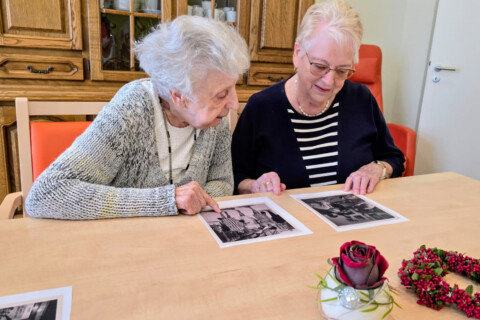Zwei ältere Frauen betrachten schwarz-weiß Fotografien, die vor Ihnen auf einem Tisch liegen